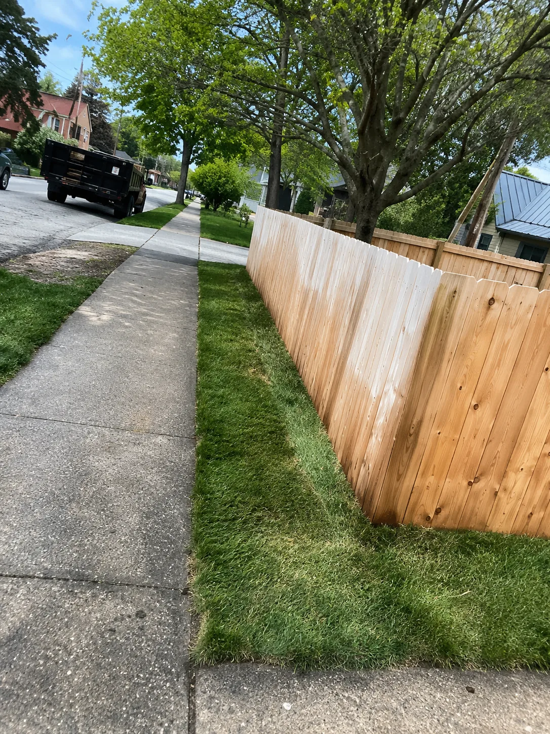 Sidewalk and property edge beside a finished wood fence and trimmed lawn