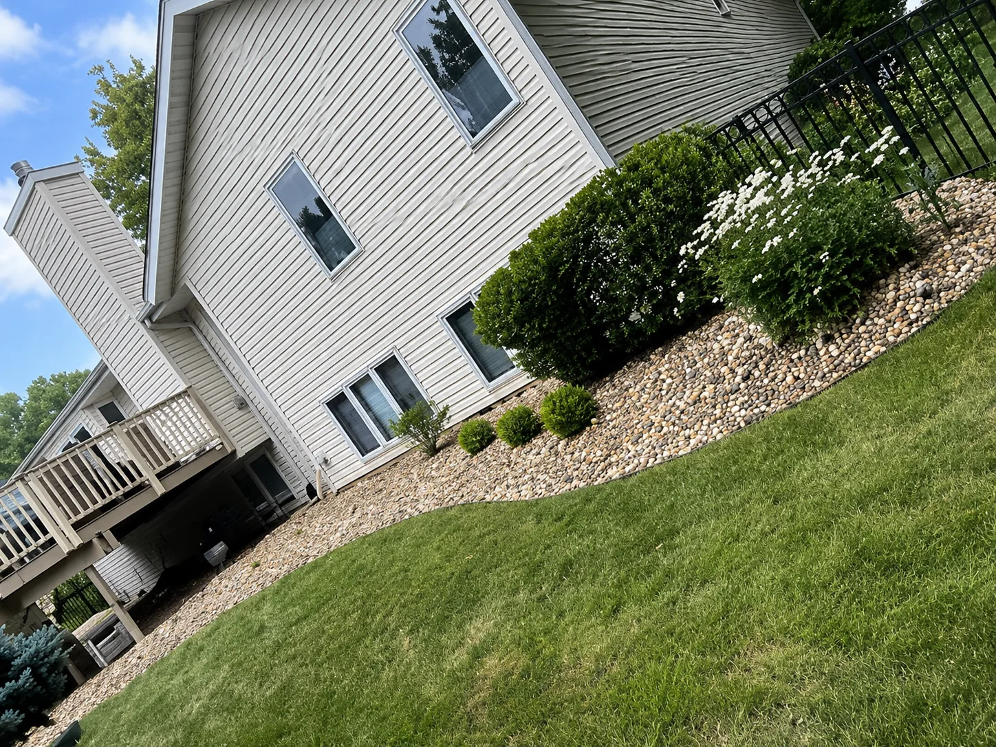 Residential yard landscaping with rock beds, shrubs, and green lawn